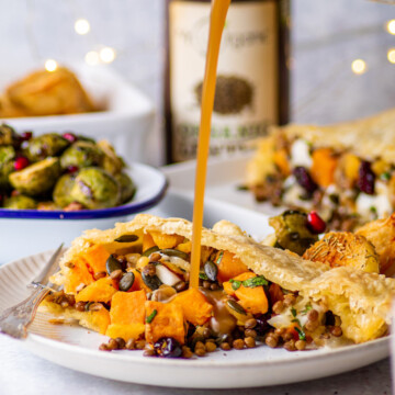a slice of vegan lentil wellington on a white plate with gravy drizzled on it