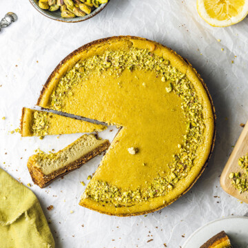 round vegan pistachio cheesecake with 2 slices cut out of it