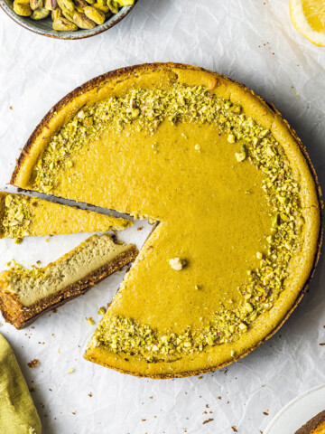 round vegan pistachio cheesecake with 2 slices cut out of it