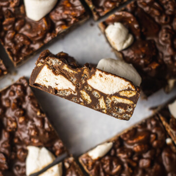 vegan chocolate rocky road slices on parchment paper with one slice in the middle flipped up showing all the crunchy layers of the vegan rocky road