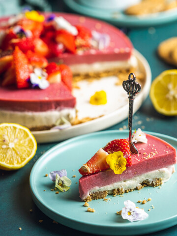 a slice of vegan strawberry cheesecake on a blue plate with the rest of the cake in the background