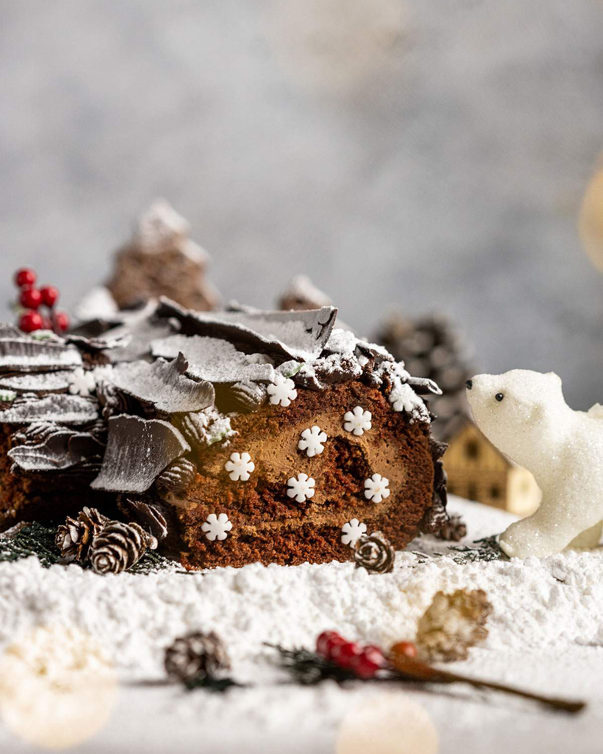 Vegan Yule Log with Chocolate bark sprinkled in icing sugar with fairy lights and a tiny polar bear next to it