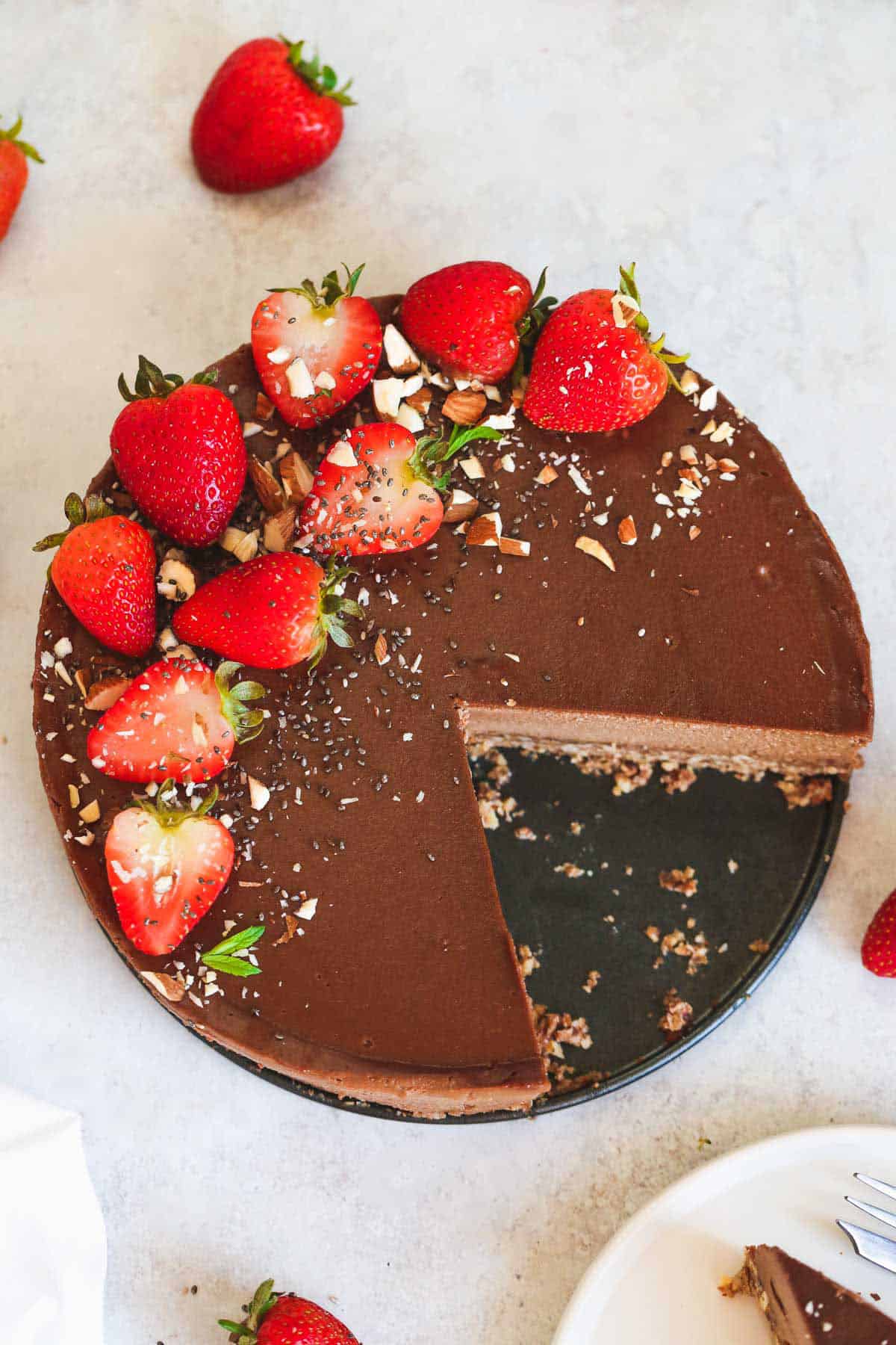 a round vegan chocolate cheesecake with 2 slices cut out at the bottom right. We can see the cake from above and it's decorated with fresh strawberries on the top left edge.