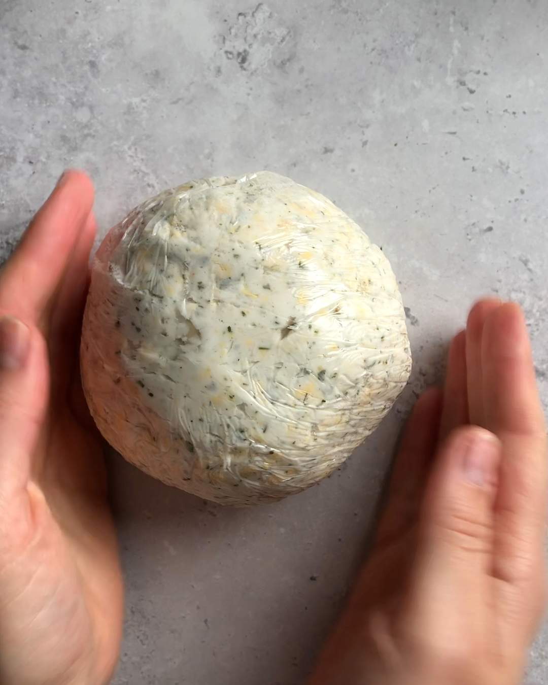 a cheese ball formed with hands, wrapped in plastic wrap