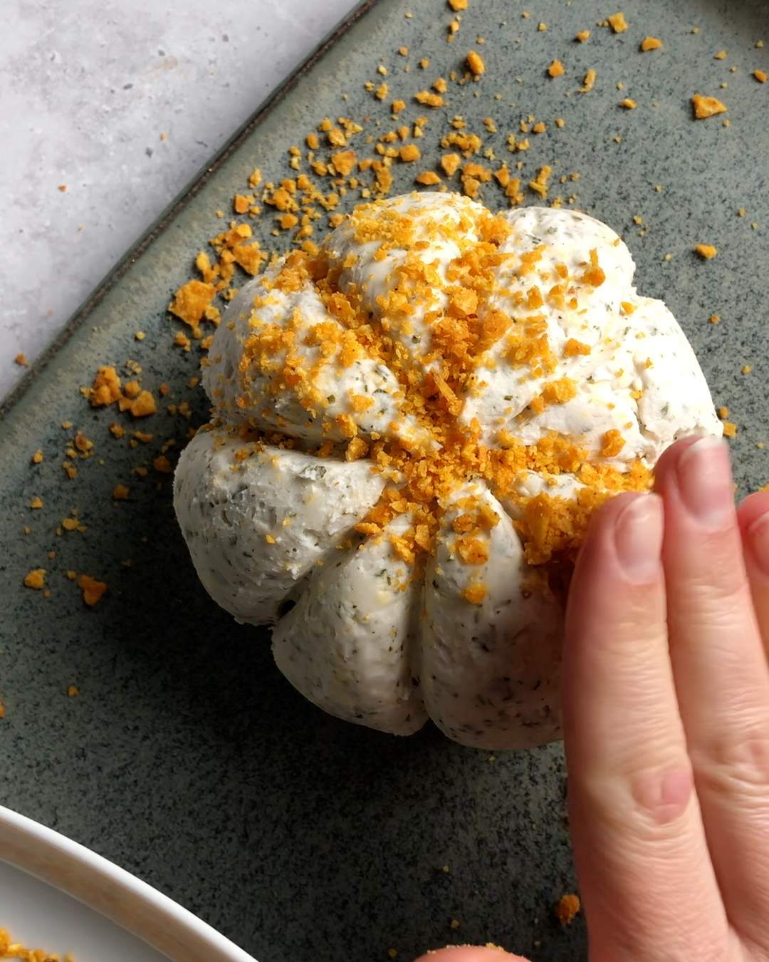 a hand patting crushed tortilla chips onto a pumpkin cheese ball