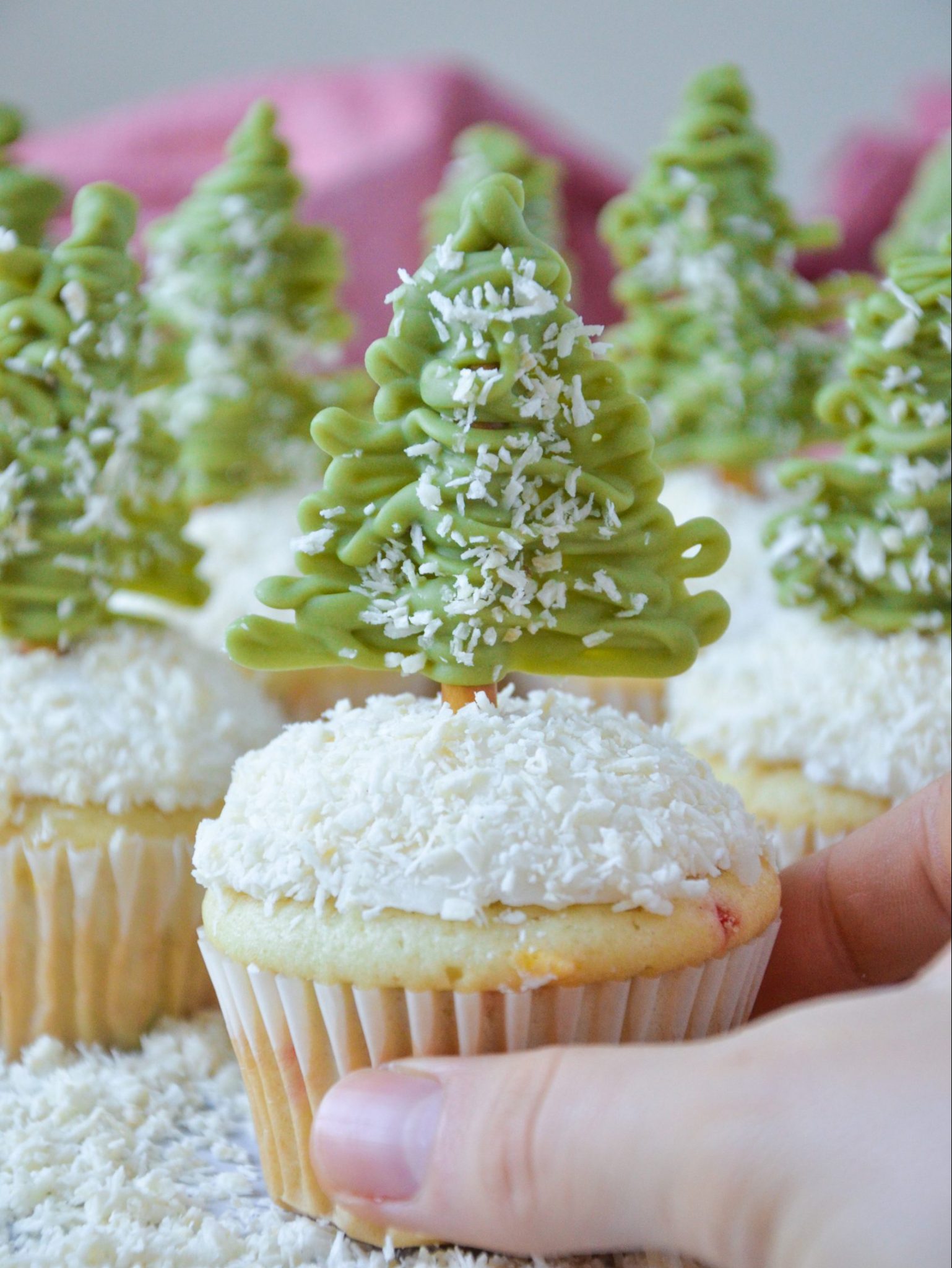 light colored vegan cupcakes with white frosting that looks like snow and dusted green christmas trees on top