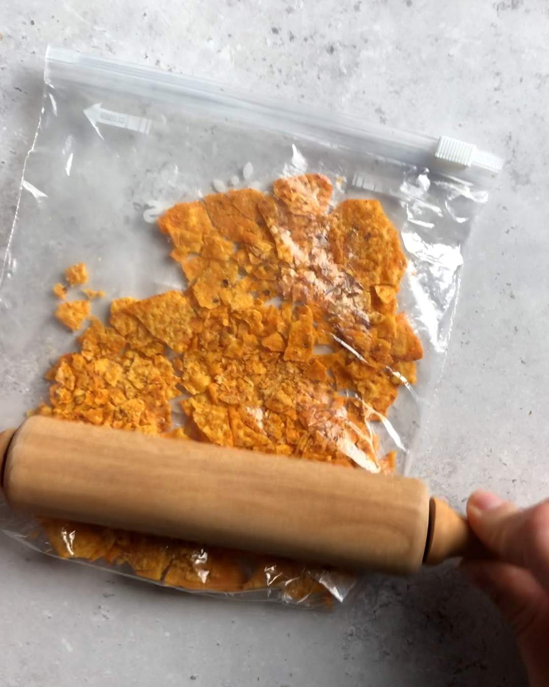 dorito tortilla chips in a freezer bag being crushed by a rolling pin