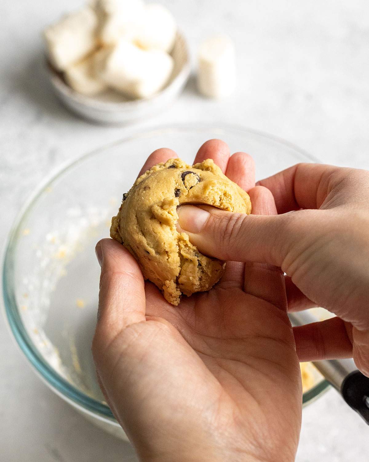 holding a cookie dough ball in one hand whilst pressing a thumb into the middle of the dough