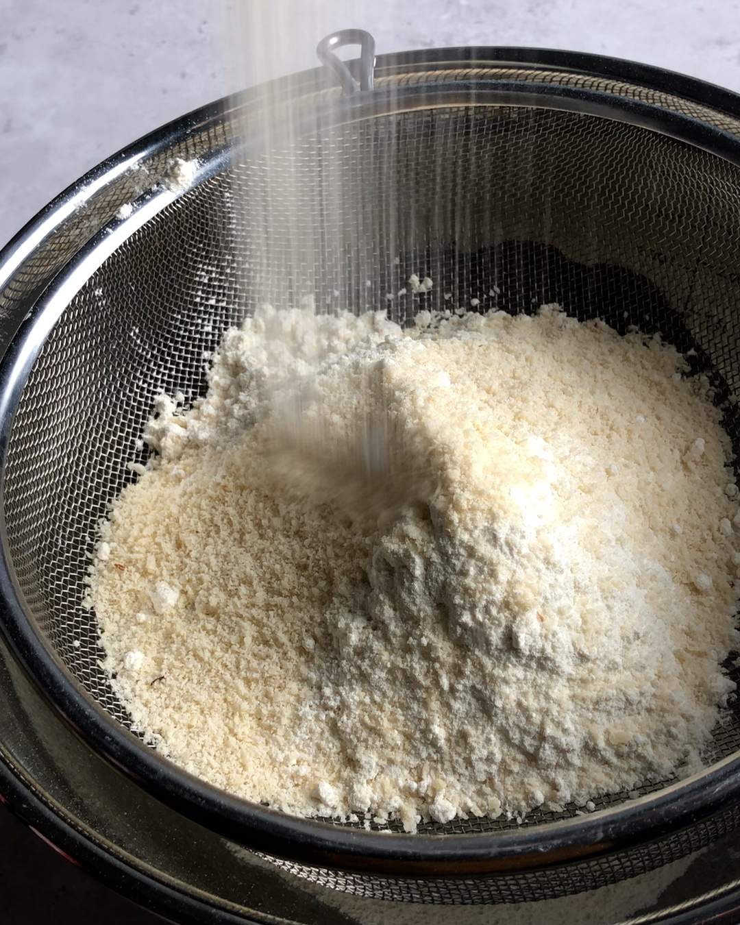 mixing dry ingredients in a sieve above a mixing bowl