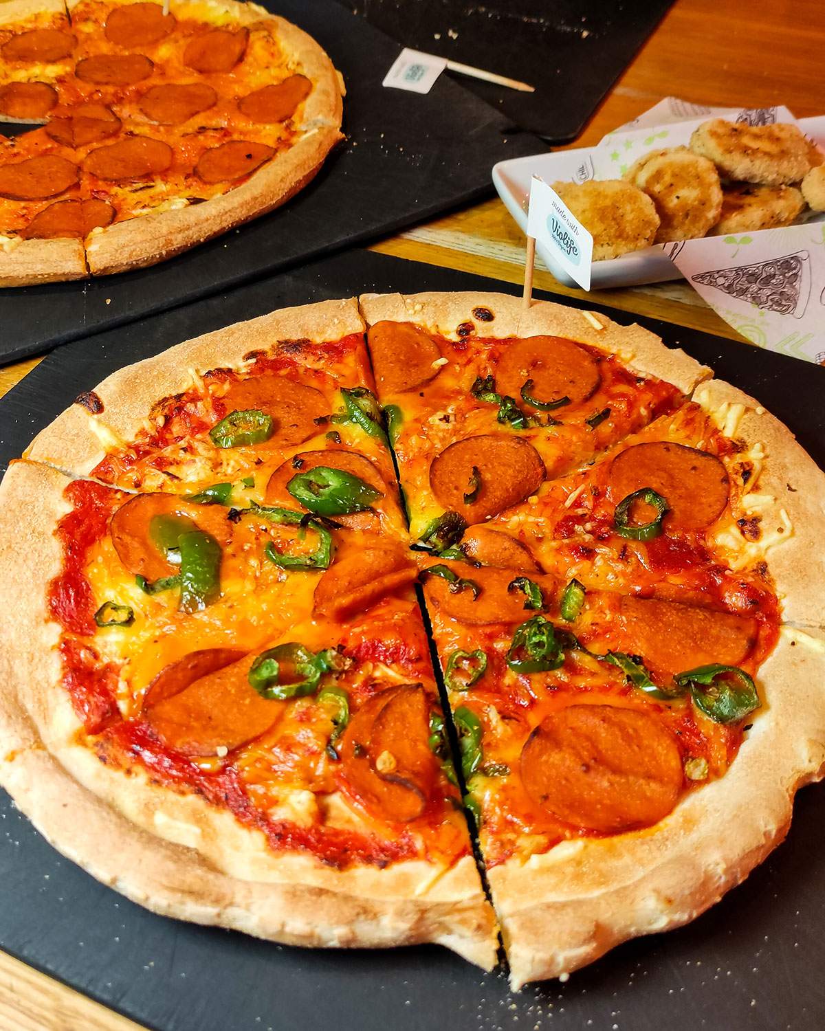 vegan pepperponi pizza on a table at pizza hut with vegan nuggets and another pizza in the background