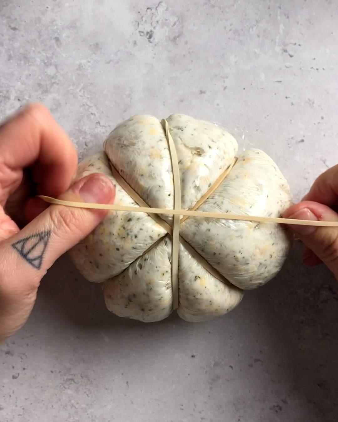 rubber bands being added to the wrapped cheese ball to create the pumpkin shape 2