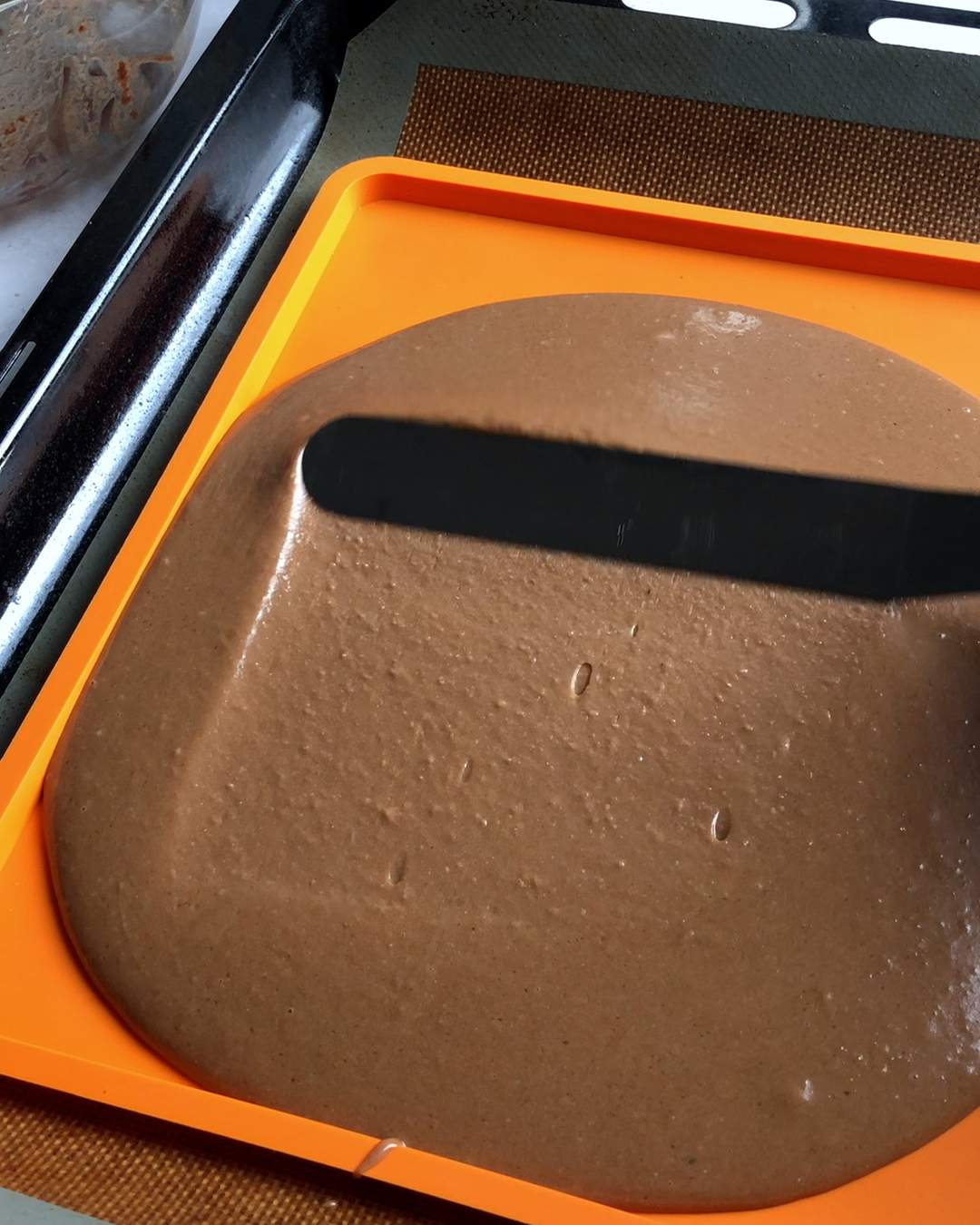 spreading chocolate cake mix across a swiss roll tray