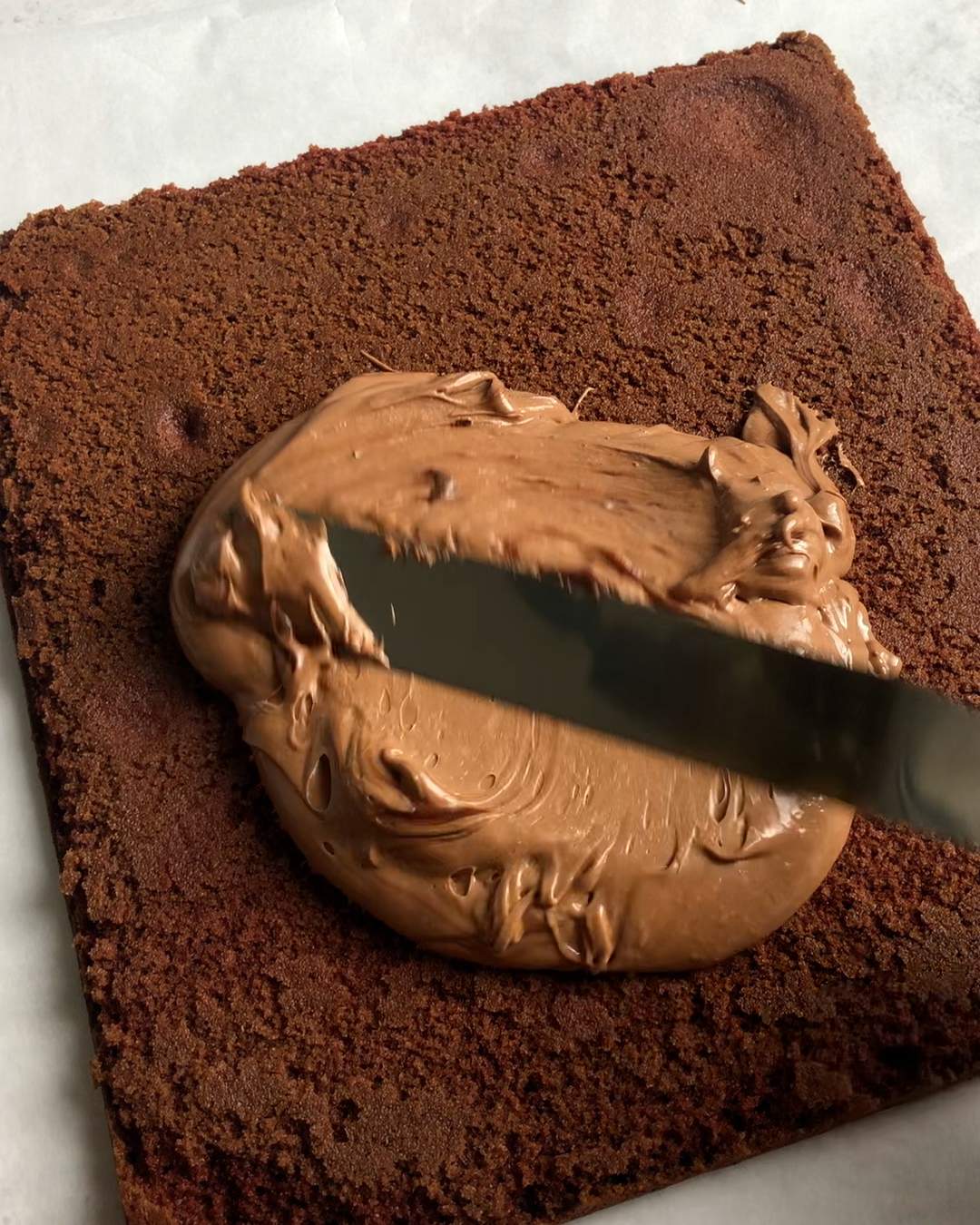 spreading vegan chocolate ganache across sponge cake