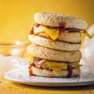 Two vegan egg McMuffins are stacked on a white plate on a yellow table.