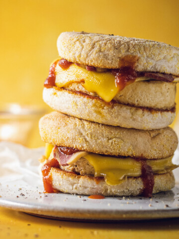 Two vegan egg McMuffins are stacked on a white plate on a yellow table.