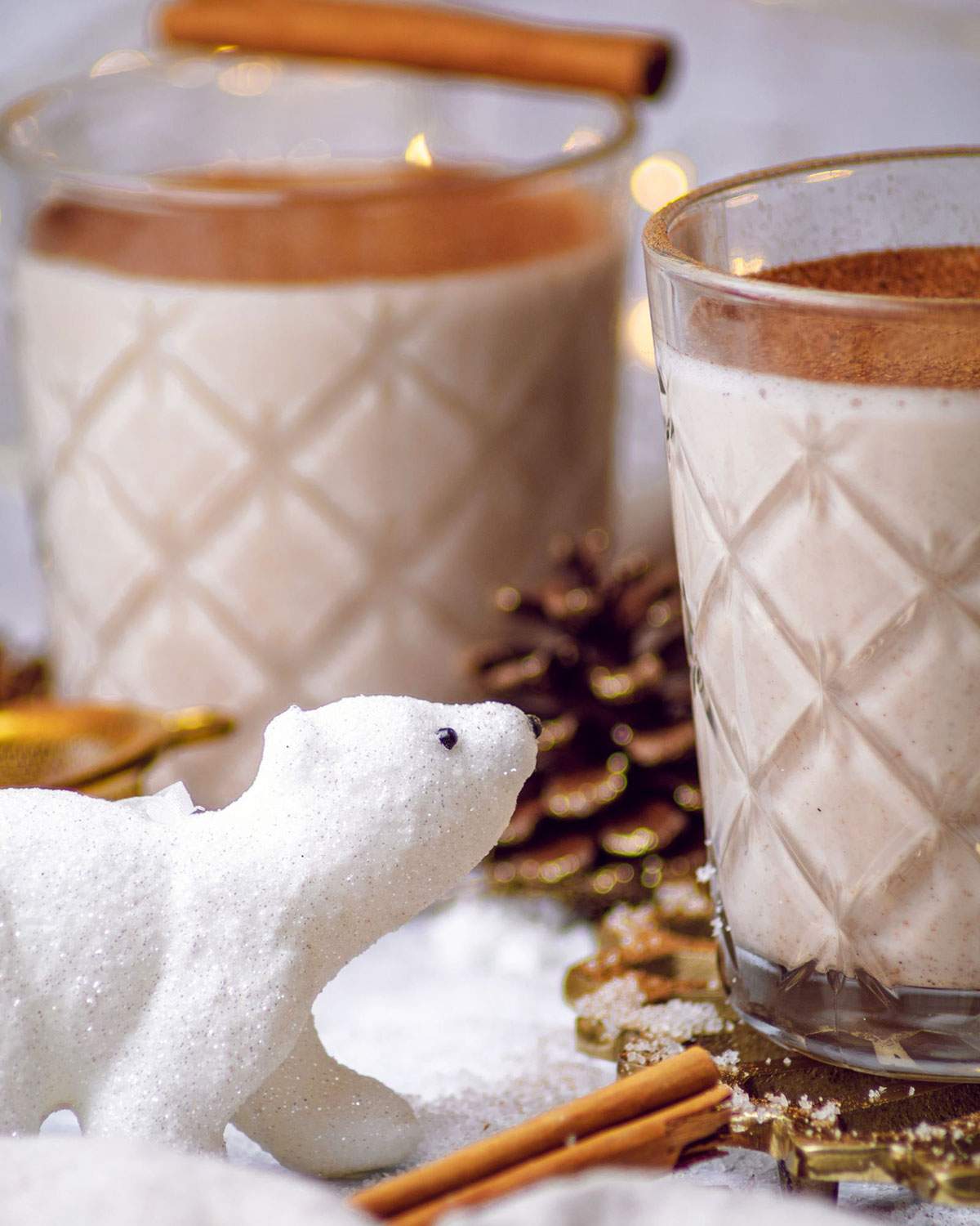 A cute little polar bear figure is looking at 2 glasses of vegan oat nog.