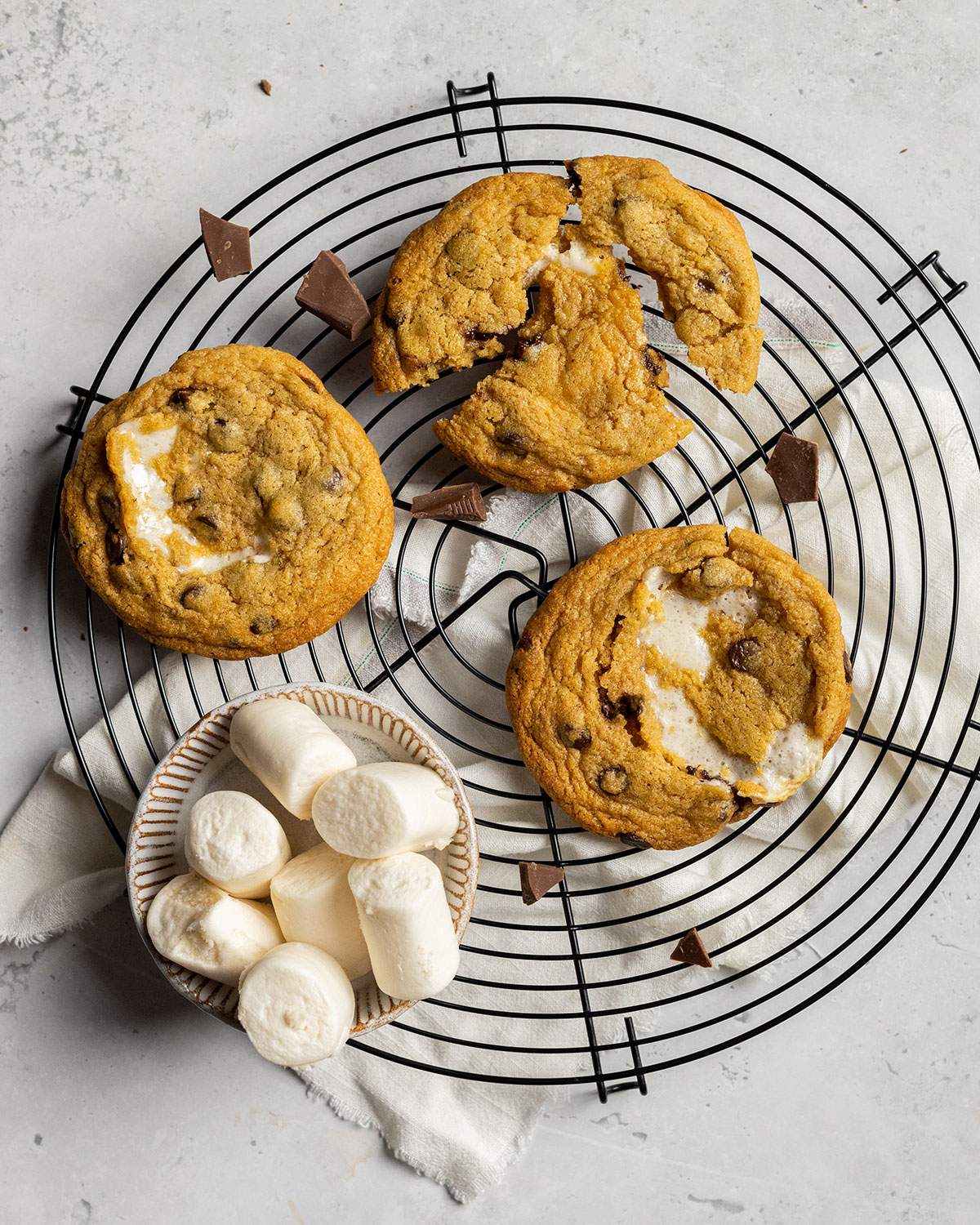 three vegan s'mores cookies and a bowl of vegan marshmallows on a cooling rack