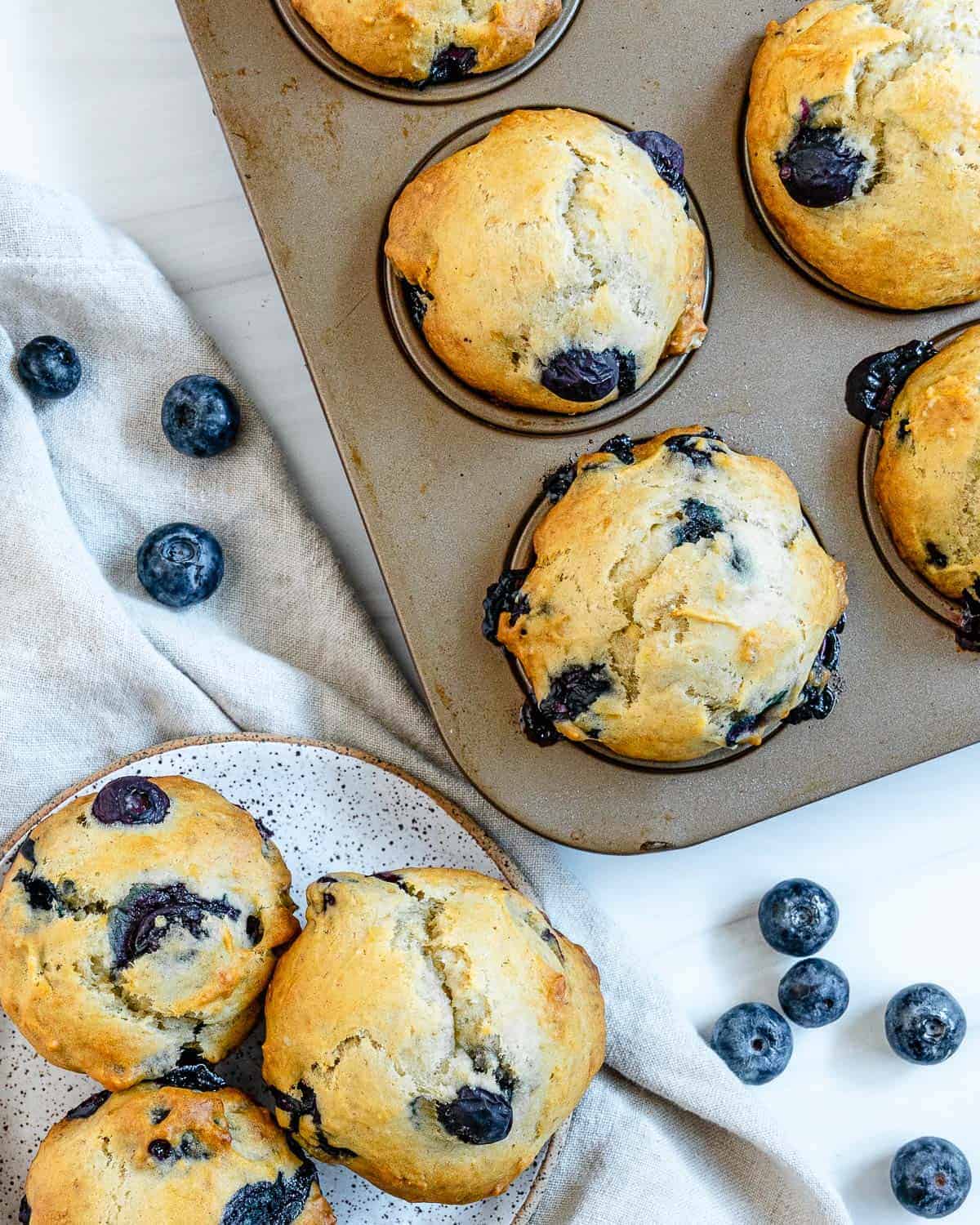 Vegan blueberry muffins in a muffin tray and on a small place next to it surrounded by blueberries