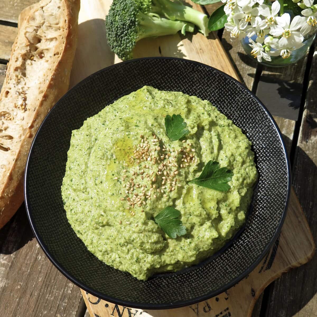 a black bowl filled with green broccoli hummus on the dining table
