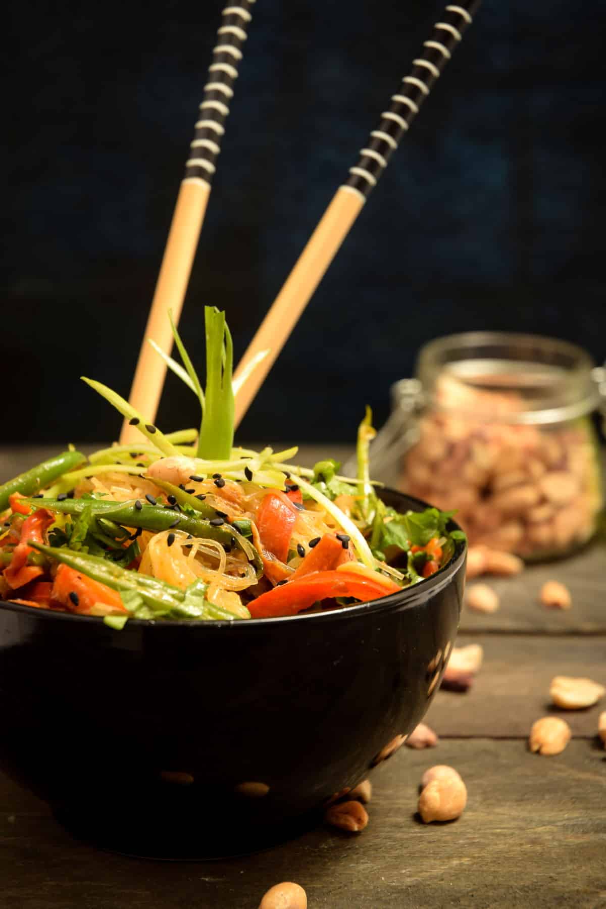 a black bowl filled with vegan pad thai and two chopsticks sticking out of it