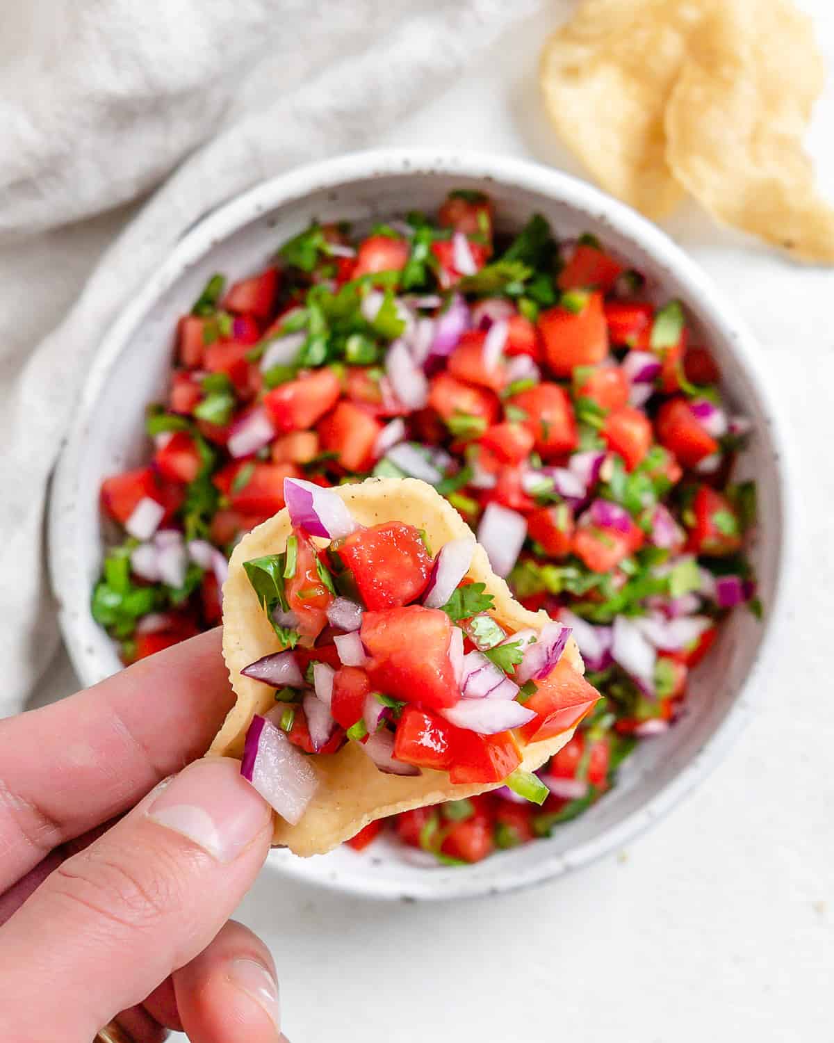 a hand scooping vegan pico de gallo out of a bowl with a chip