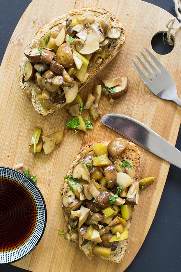 two slices of bread topped with cooked mushrooms on a wooden serving board