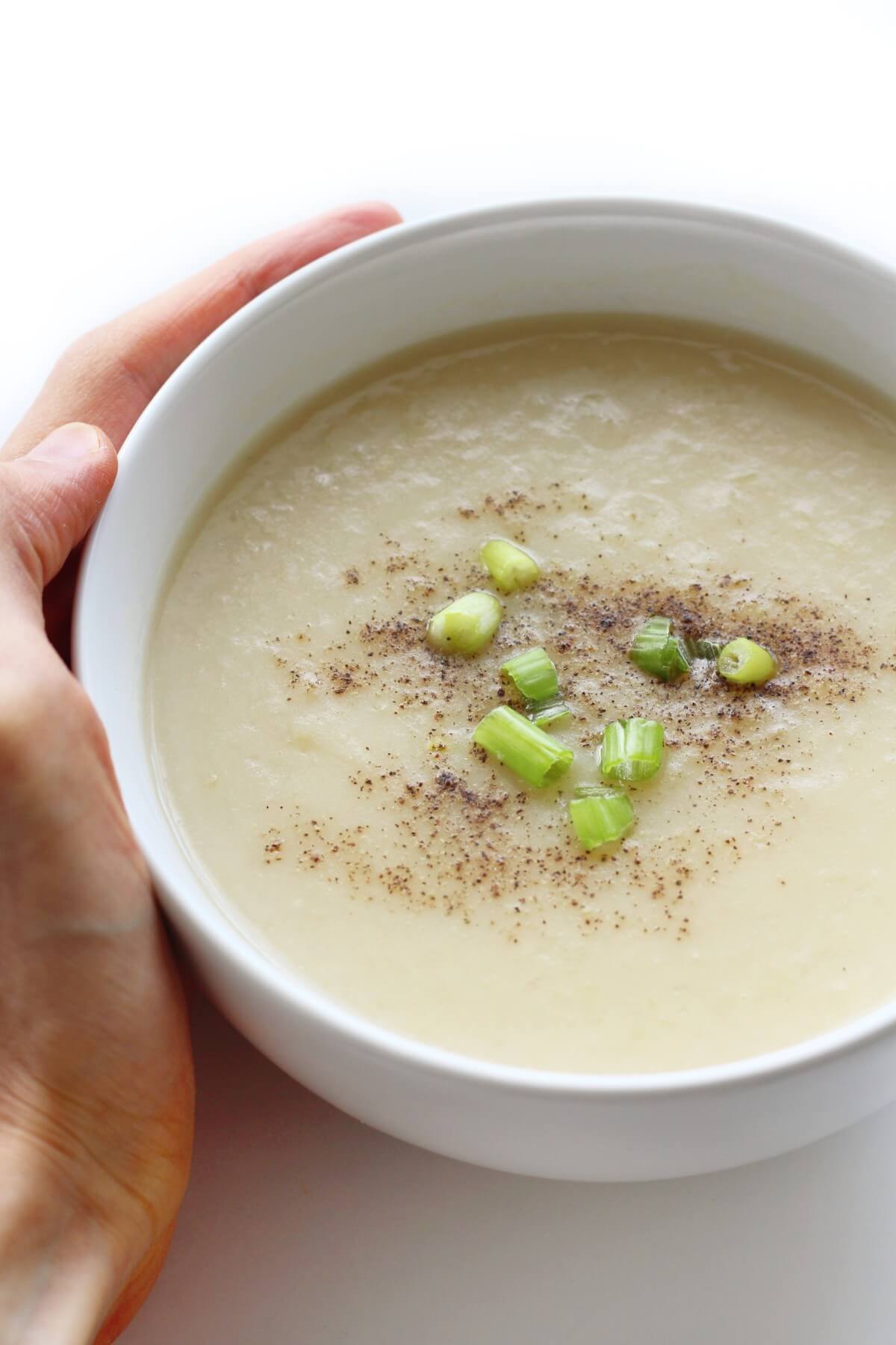 creamy vegan potato soup topped with green onions in a white bowl