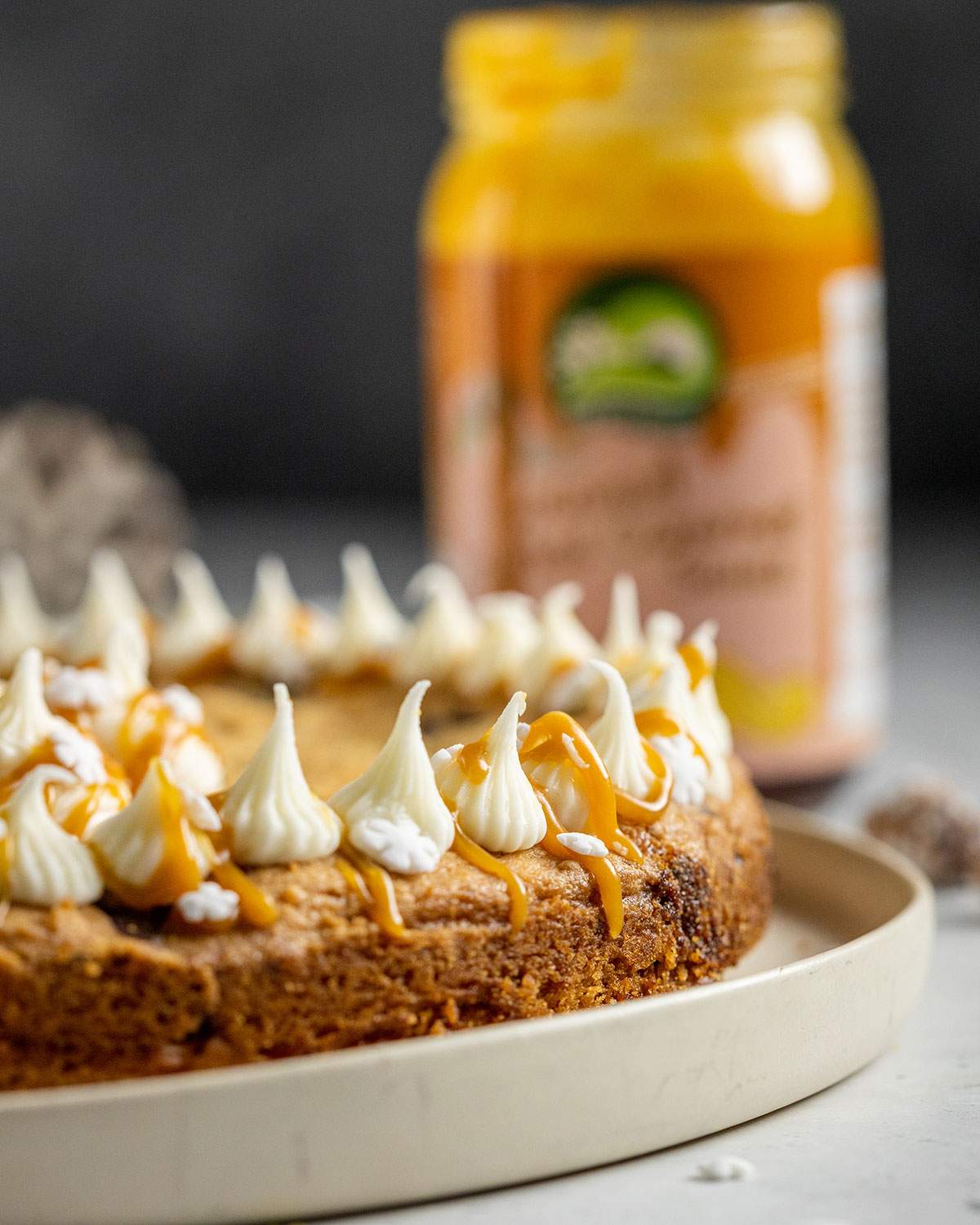 a round vegan cookie cake topped with vegan frosting and salted caramel sauce on a white table