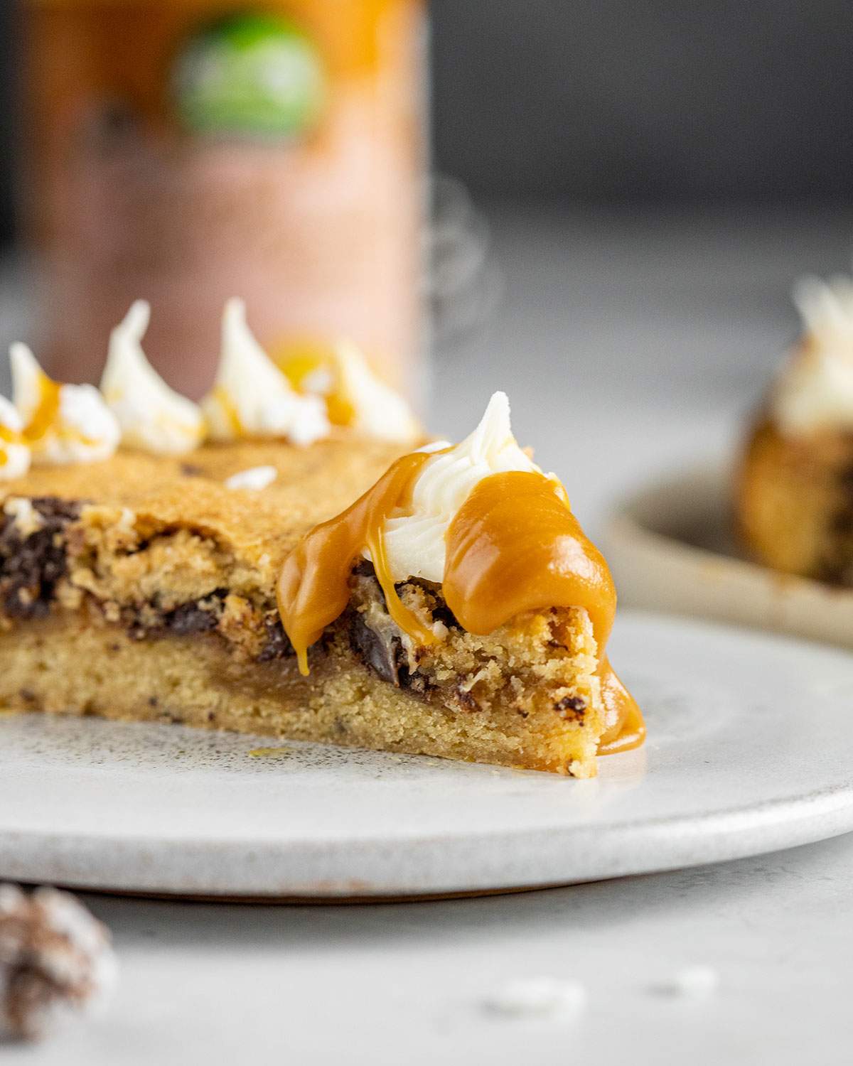 a slice of vegan chocolate chip cookie cake with vegan frosting and vegan caramel sauce