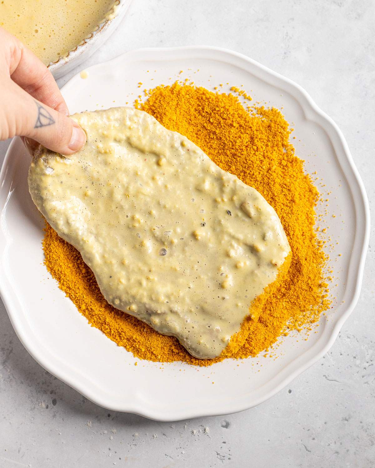 coating a vegan seitan schnitzel in breadcrumbs on a plate