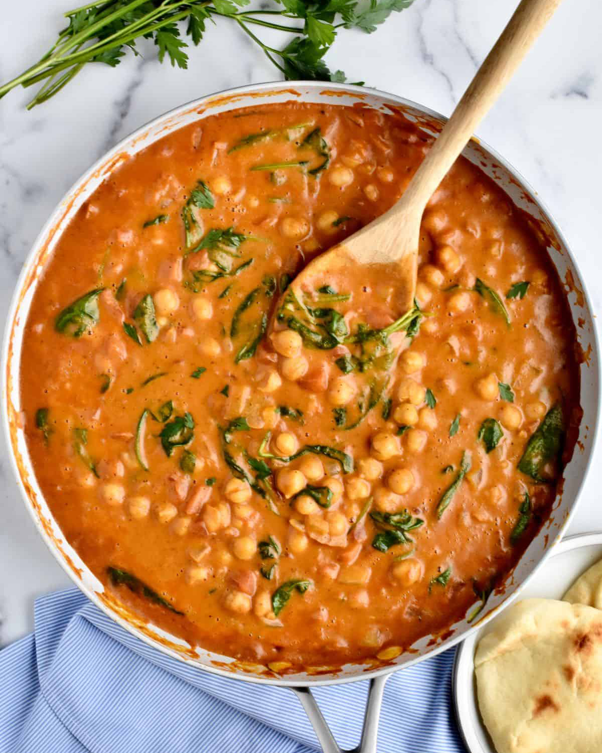 a large skillet filled with chickpea spinach curry and a wooden spoon on the side