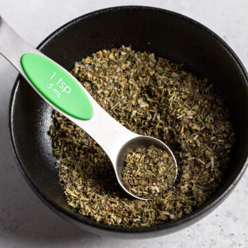vegan poultry seasoning in a black bowl with a small measuring spoon