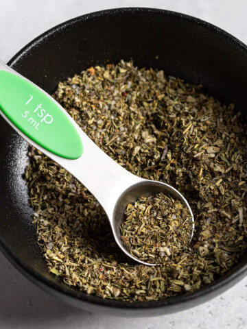 vegan poultry seasoning in a black bowl with a small measuring spoon
