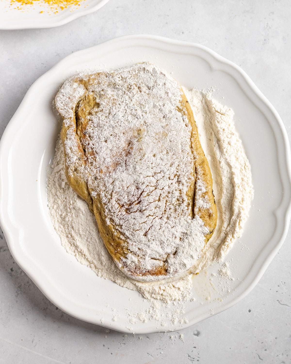 coating a vegan schnitzel in flour on a white plate