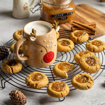 vegan thumbvegan thumbprint cookies with apple pie jam on a cooling rack next to a reindeer shaped mug
