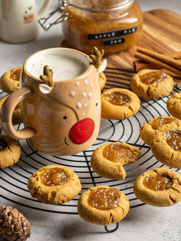 vegan thumbvegan thumbprint cookies with apple pie jam on a cooling rack next to a reindeer shaped mug