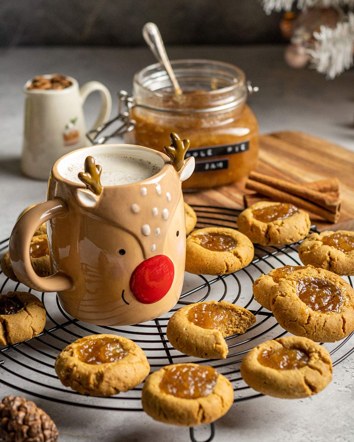 a cooling rack covered with vegan thumbprint cookies and a cosy mug, one cookie has a bite taken out of it