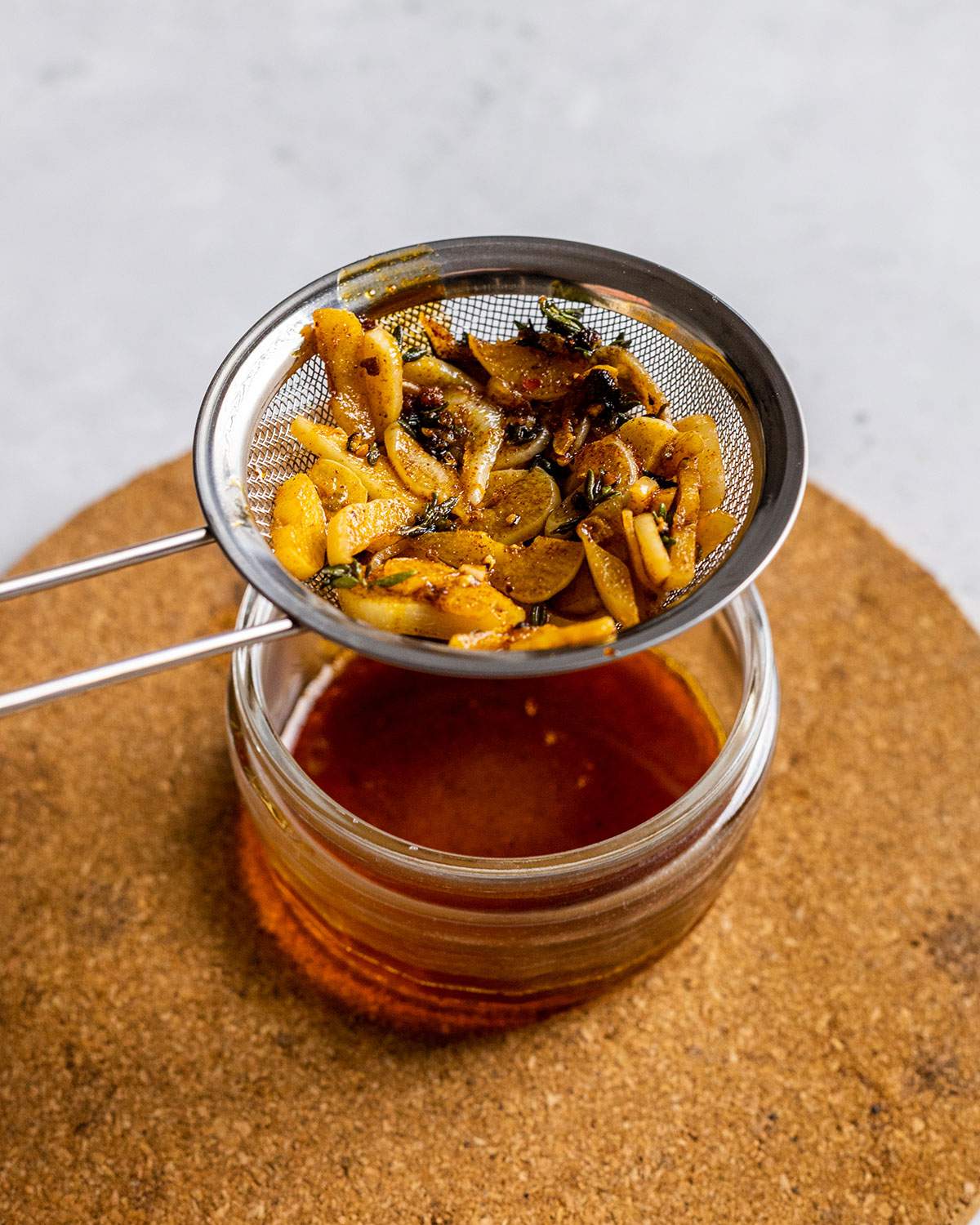 garlic and herbs in a fine mesh sieve over a small bowl of flavor oil