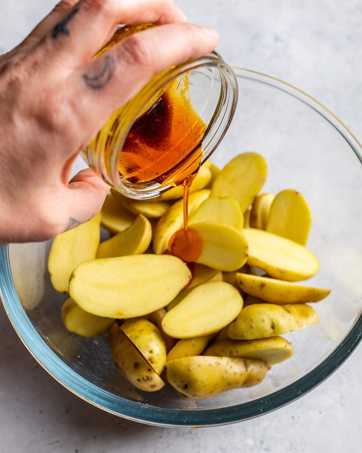 pouring flavor oil from a small jar onto fingerling potato halves in a mixing bowl