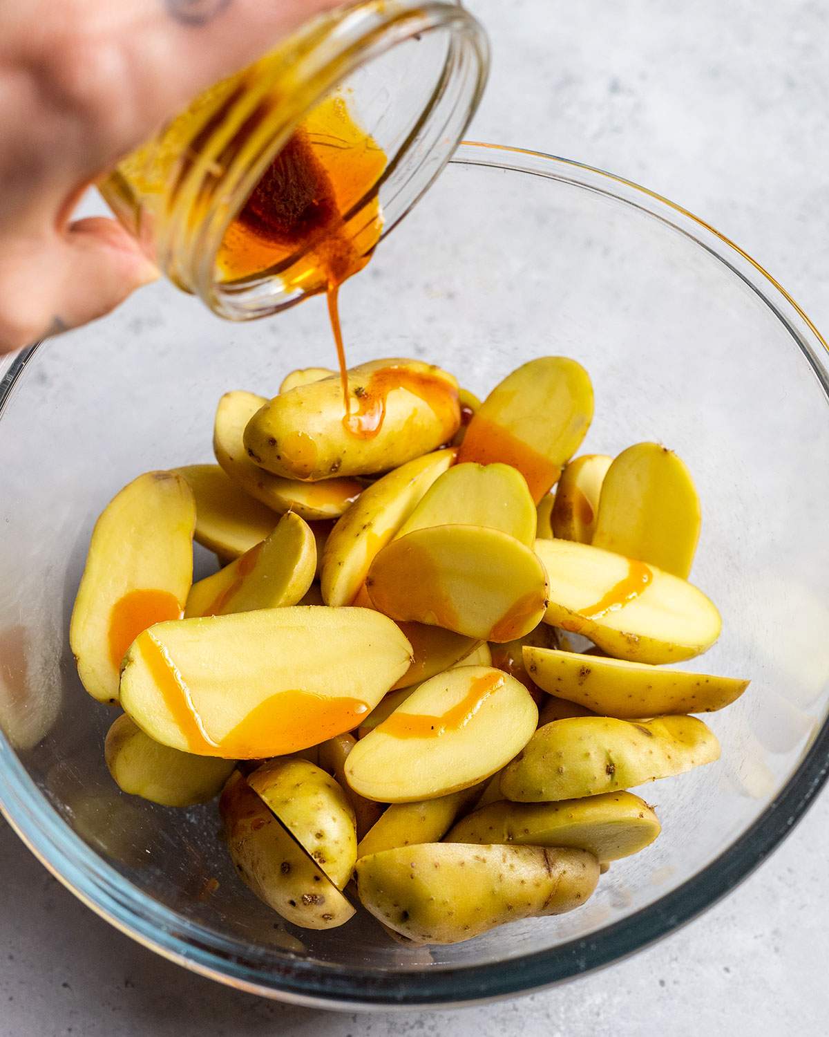 pouring flavor oil from a small jar onto fingerling potato halves in a mixing bowl