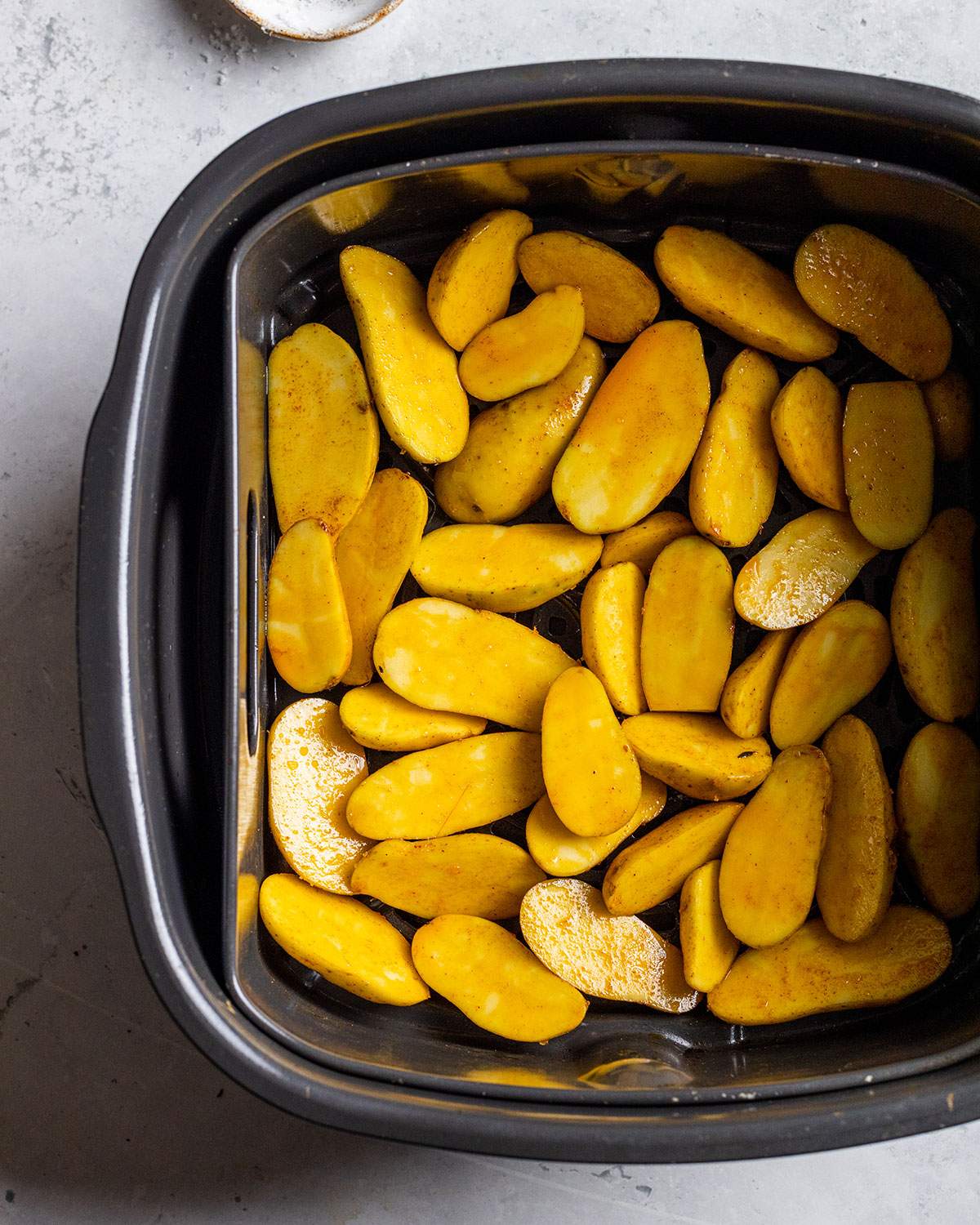 fingerling potato halves coated in flavor oil in an air fryer basket before cooking