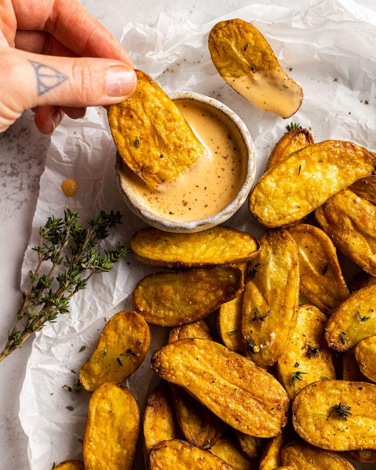 a hand dipping a fried fingerling potato into a dip