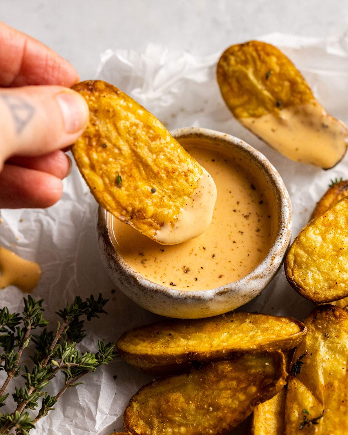 a hand dipping a fried fingerling potato into a dip