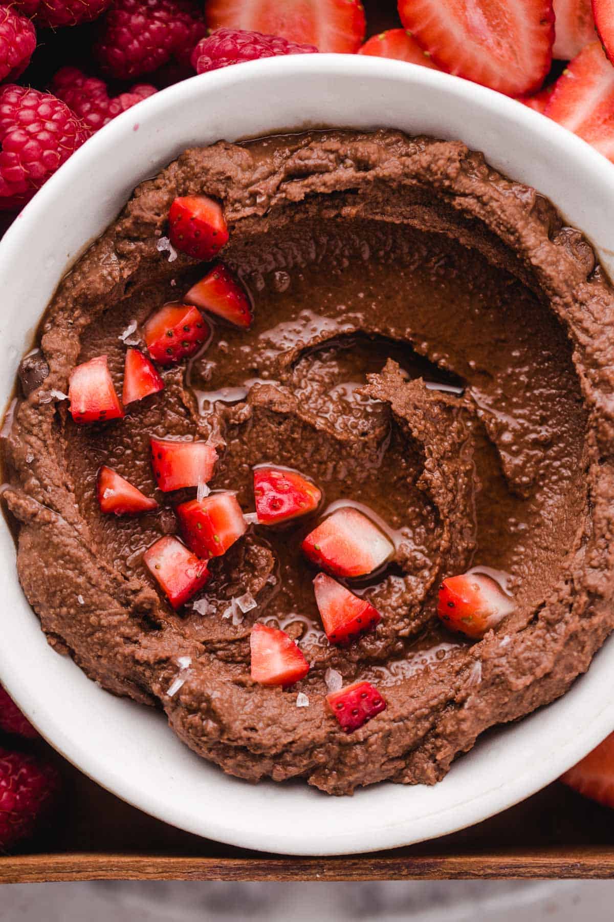 a small bowl filled with vegan brownie batter hummus and fresh fruit on top