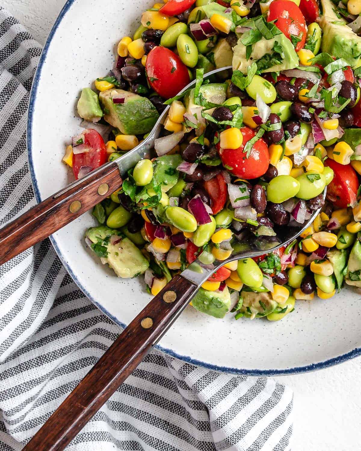 vibrant edamame salad with two spoons in a white bowl