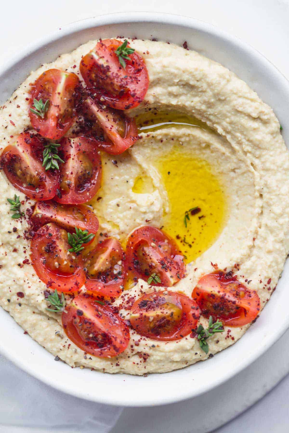 a bowl filled with creamy vegan hummus, topped with cherry tomato halves