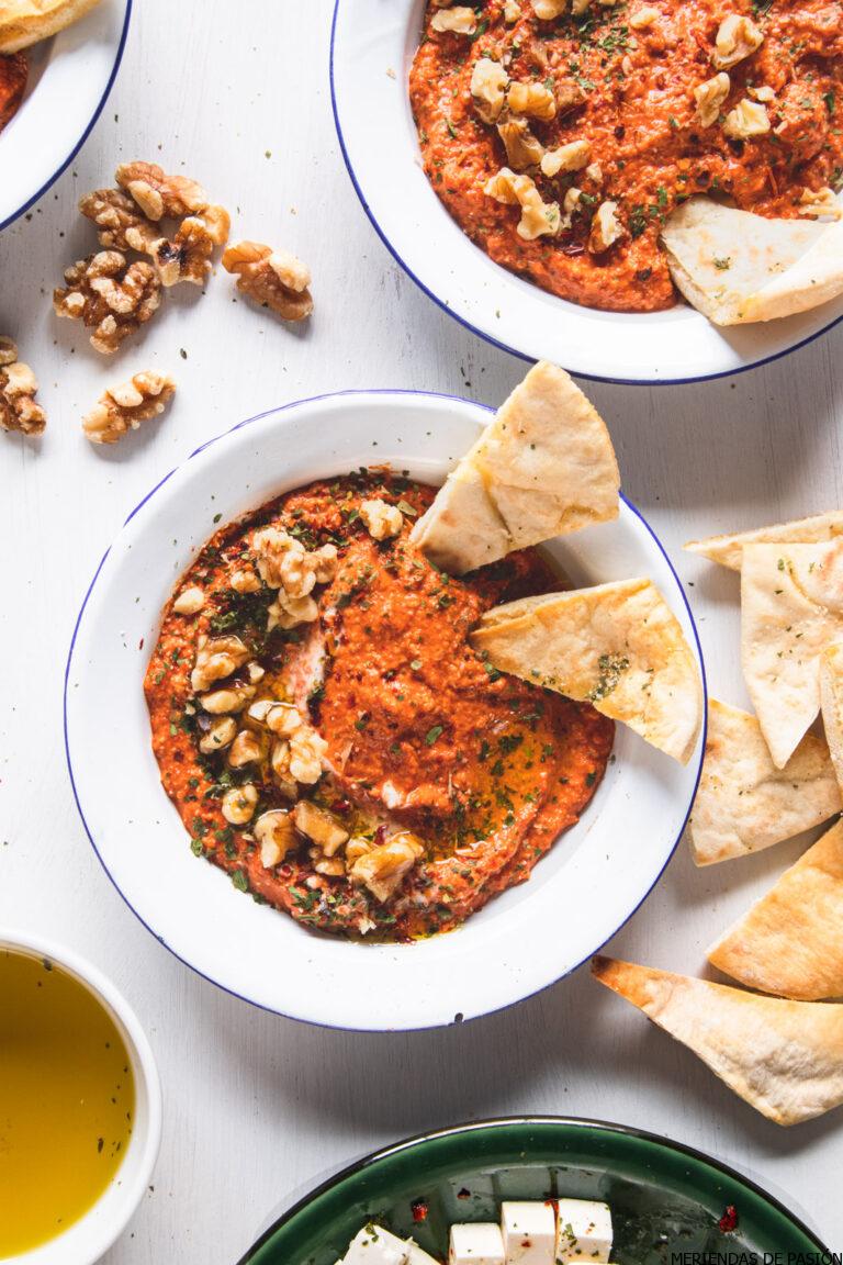 a white bowl filled with vibrant muhammara dip with pitta bread on the side