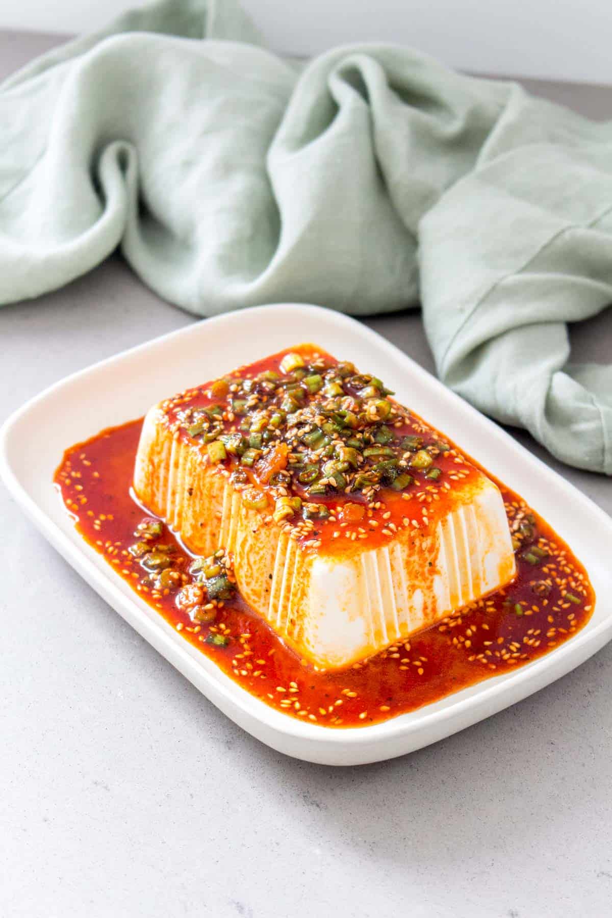 a block of silken tofu on a serving dish with soy sesame sauce on top