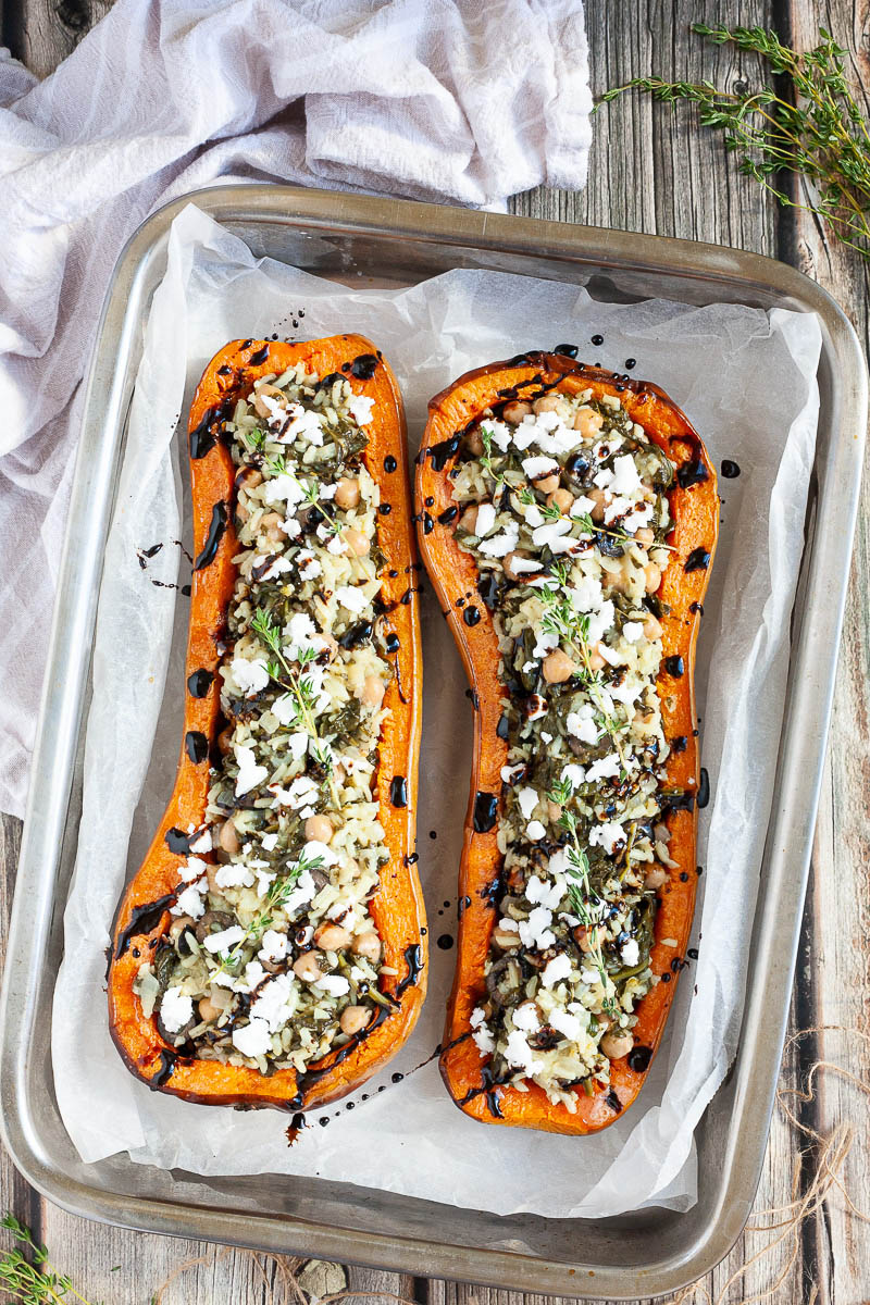 two halves of a butternut squash on an oven tray filled with mediterranean vegetables