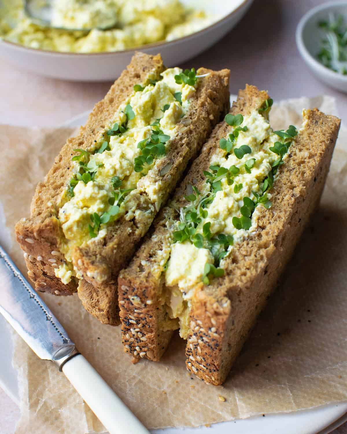 two vegan egg mayo sandwiches on a parchment paper